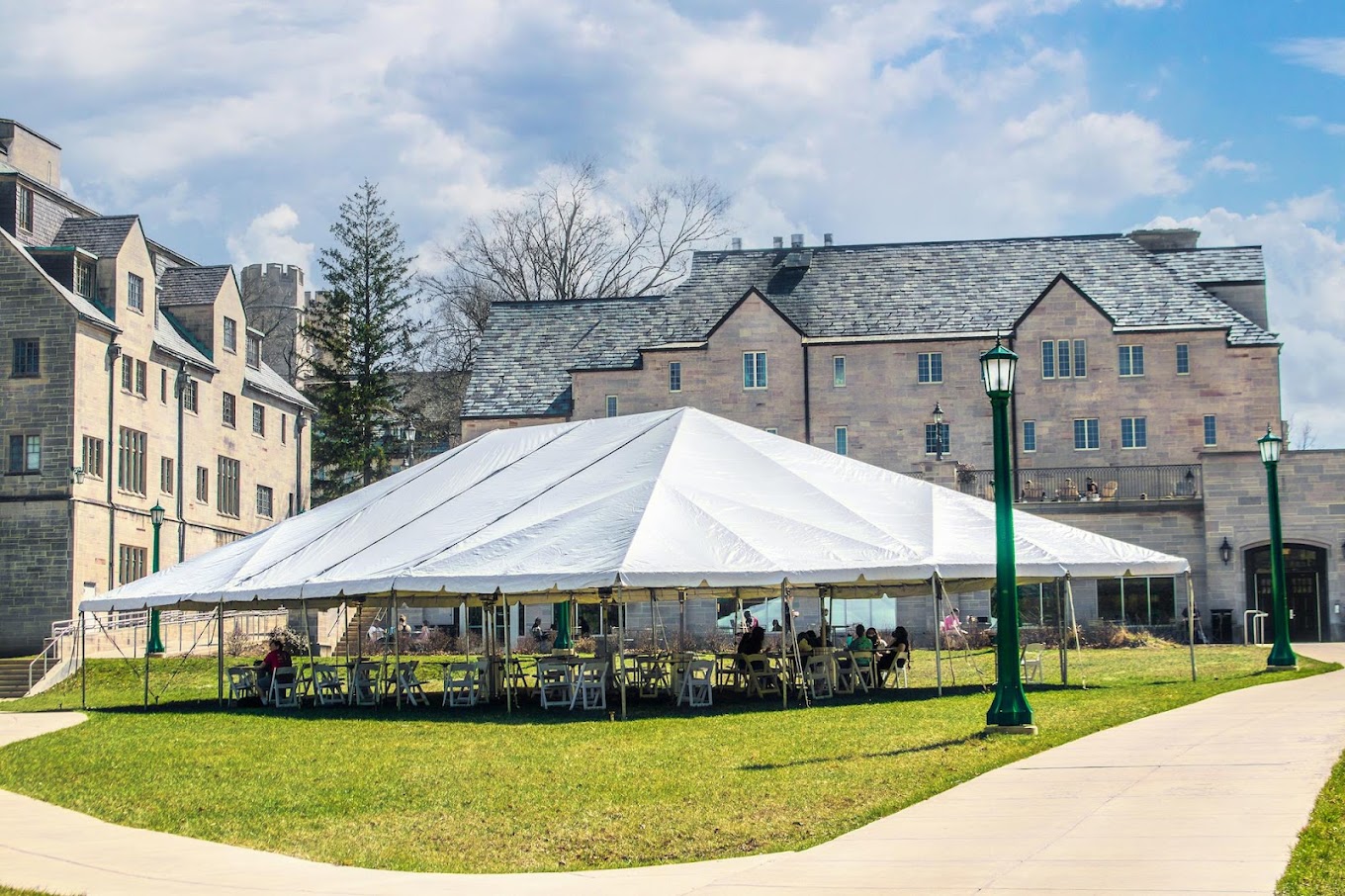 Large white pole tent on a lawn with white folding chairs