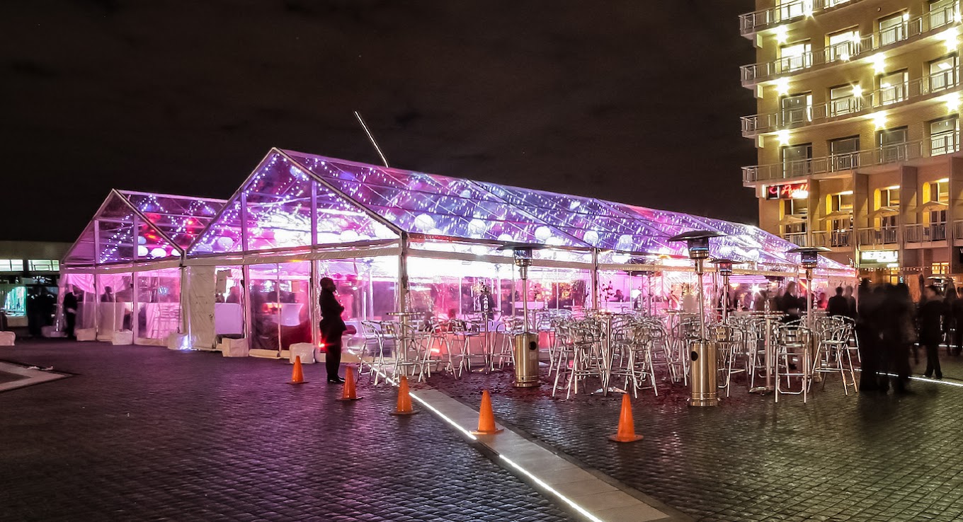 white frame tent with string lights set up in a Brooklyn backyard at dusk, tables and chairs arranged underneath