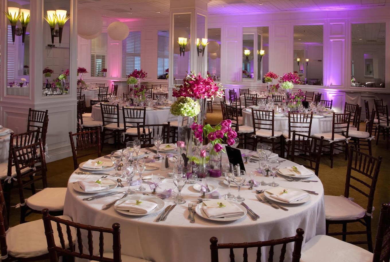 Reception room — round tables, dark chiavari chairs, floral centerpieces
